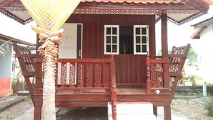 Una casa di legno tradizionale con un portico, una palma davanti e un tetto rosso.