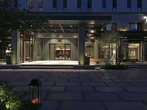 Una entrada de hotel moderna con un corredor cubierto, puertas de cristal y una fachada bien iluminada.