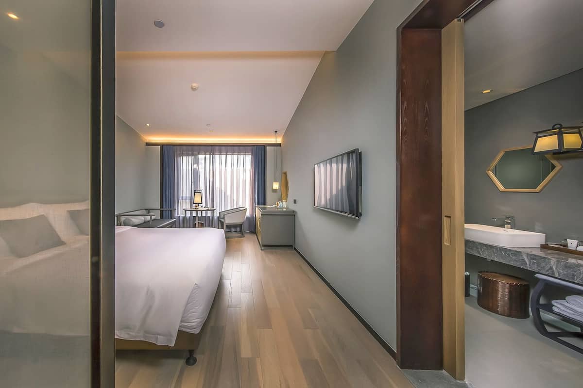A hotel room with a bed, bedside table, and a bathroom with a sink and mirror.