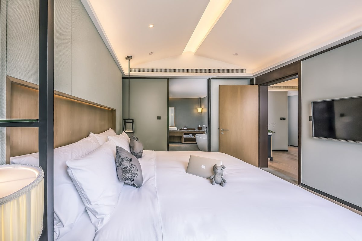 A modern hotel room with a large bed, a bedside lamp, a mirror, and a TV.