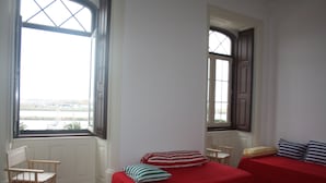 Una habitación con dos camas, una silla de madera, una mesita y una ventana con vistas al mar.