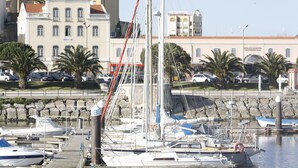 Un puerto deportivo con barcos amarrados, un muro de piedra y edificios al fondo.