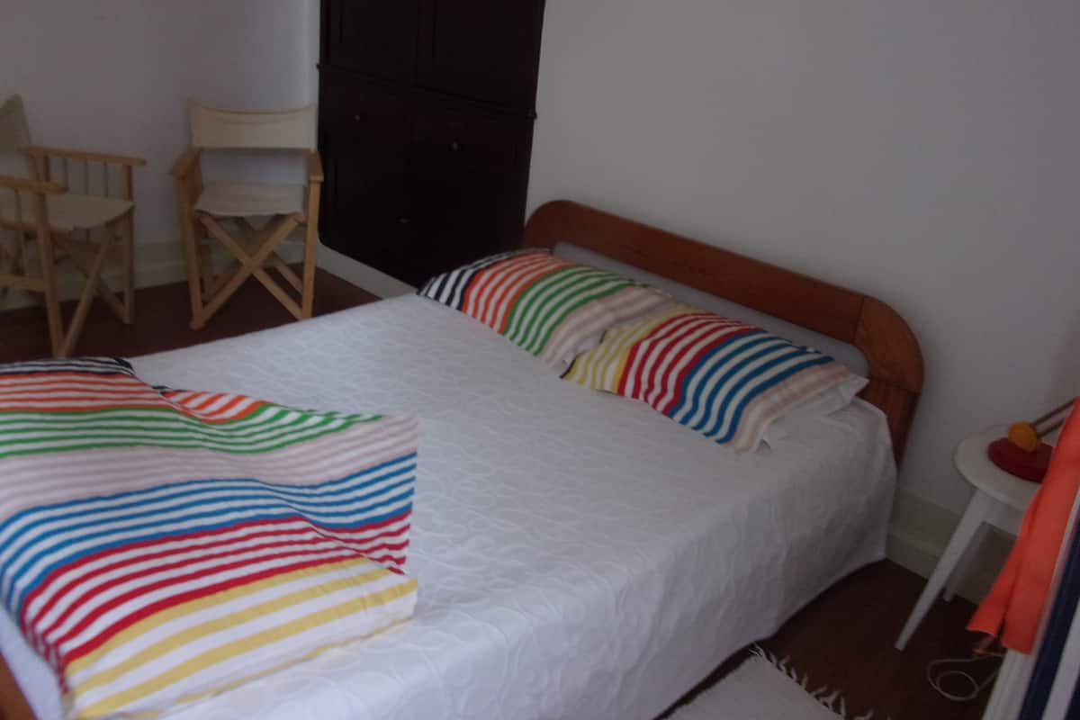 A room with a bed, two chairs, a small table, and a wardrobe.