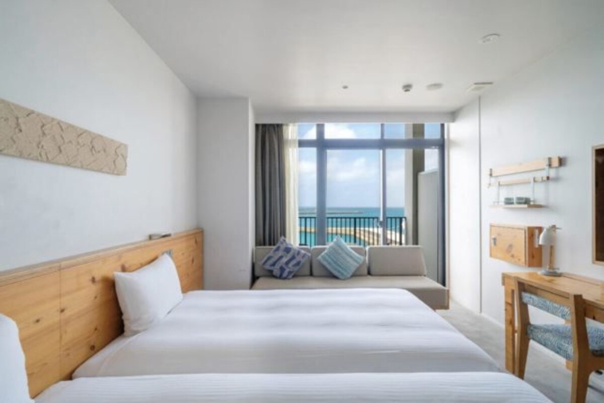 A hotel room with a large bed, a view of the ocean, a balcony with a pool, and a wooden headboard.