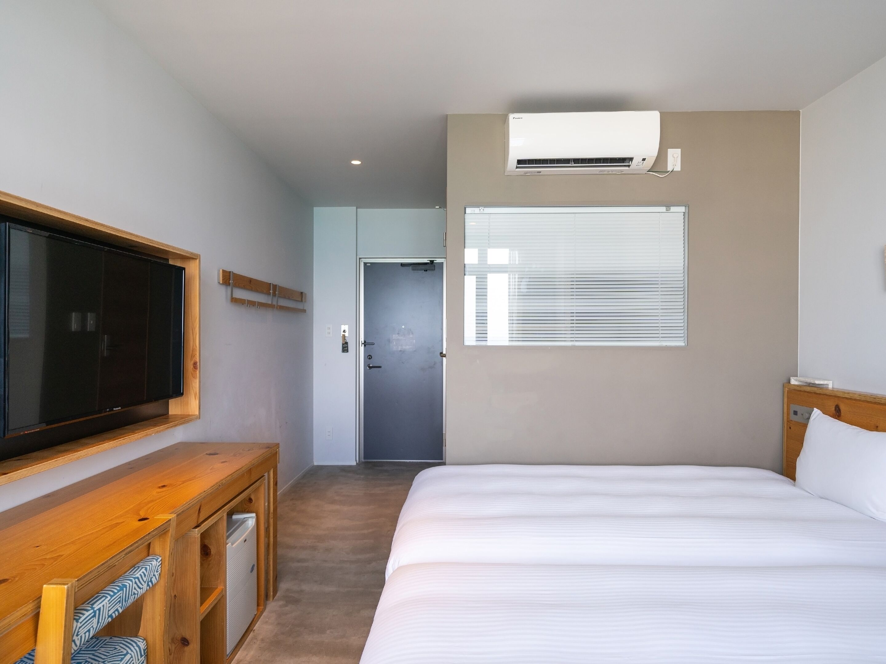 Une chambre d’hôtel équipée d’un lit, d’une télévision, d’une armoire, d’un bureau, d’un climatiseur et d’une porte donnant sur une autre pièce.