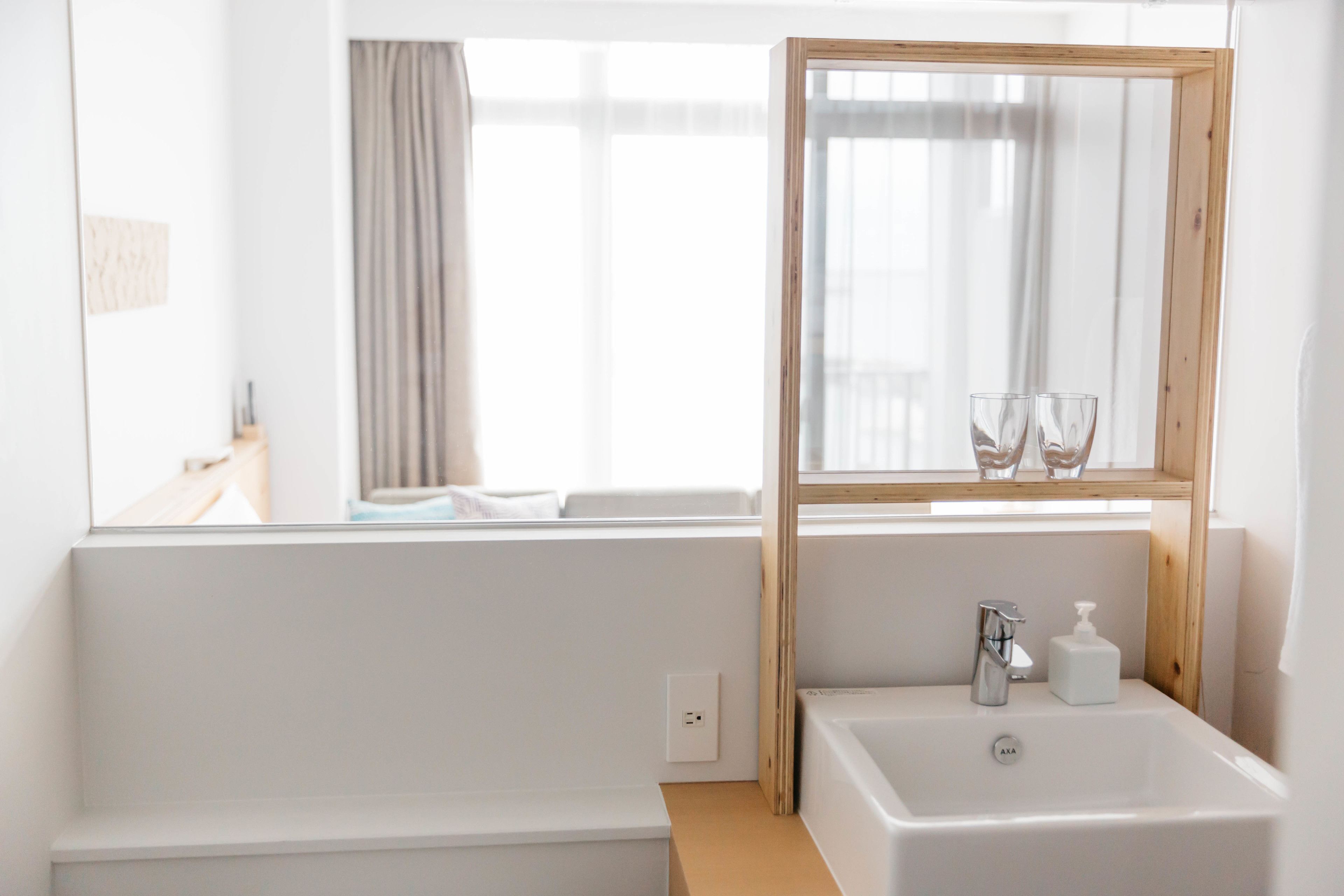 A modern bathroom with a large mirror, a sink, and a window with curtains.