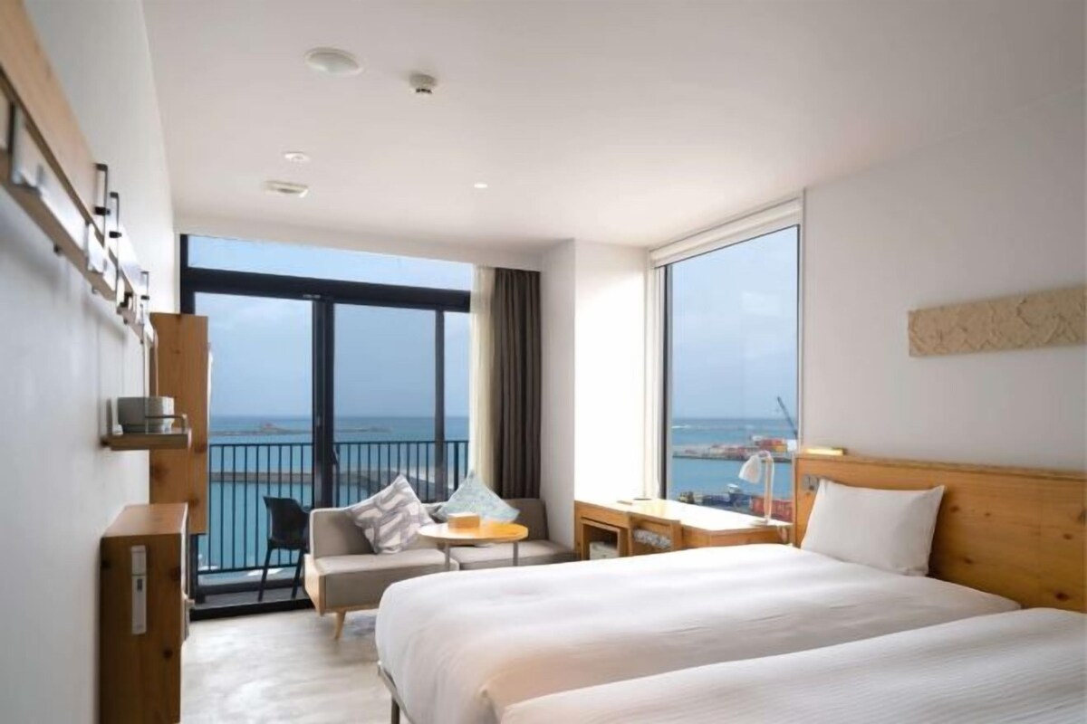 A hotel room with a large bed, a desk, a chair, and a view of the sea.