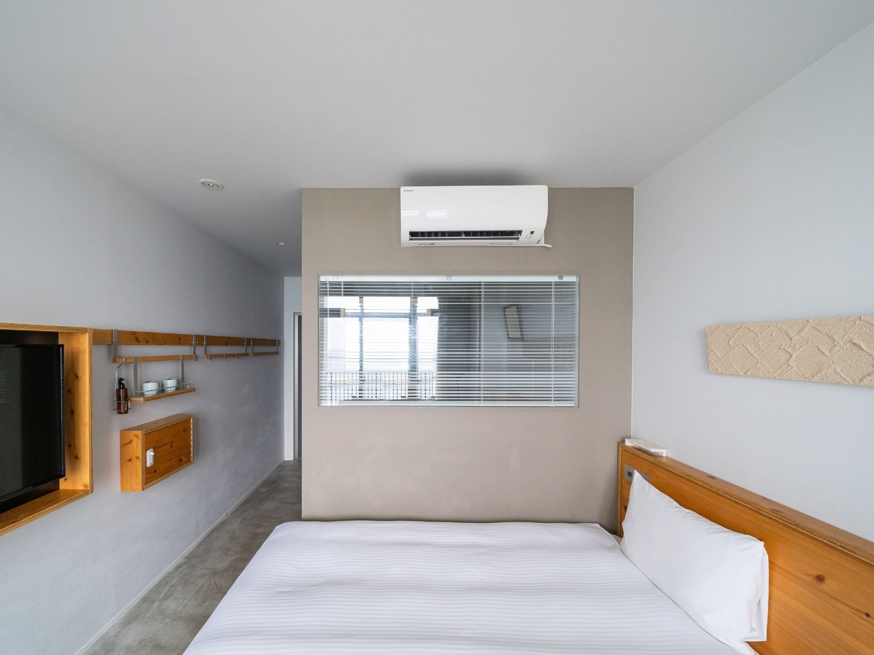 Una habitación de hotel con una cama, televisión, ventana con persianas y aire acondicionado.
