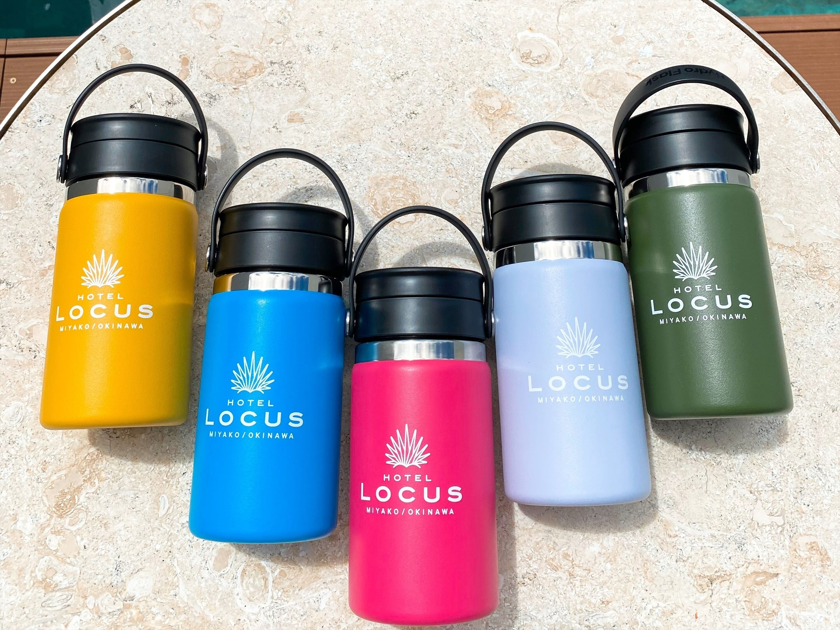 Five water bottles with the Hotel Locus logo, arranged on a textured surface.