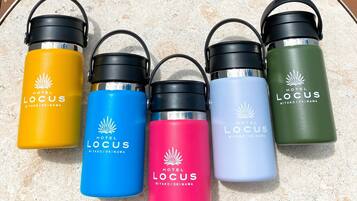 Cinq bouteilles d’eau ornées du logo de l’hôtel Locus, disposées sur une surface texturée.