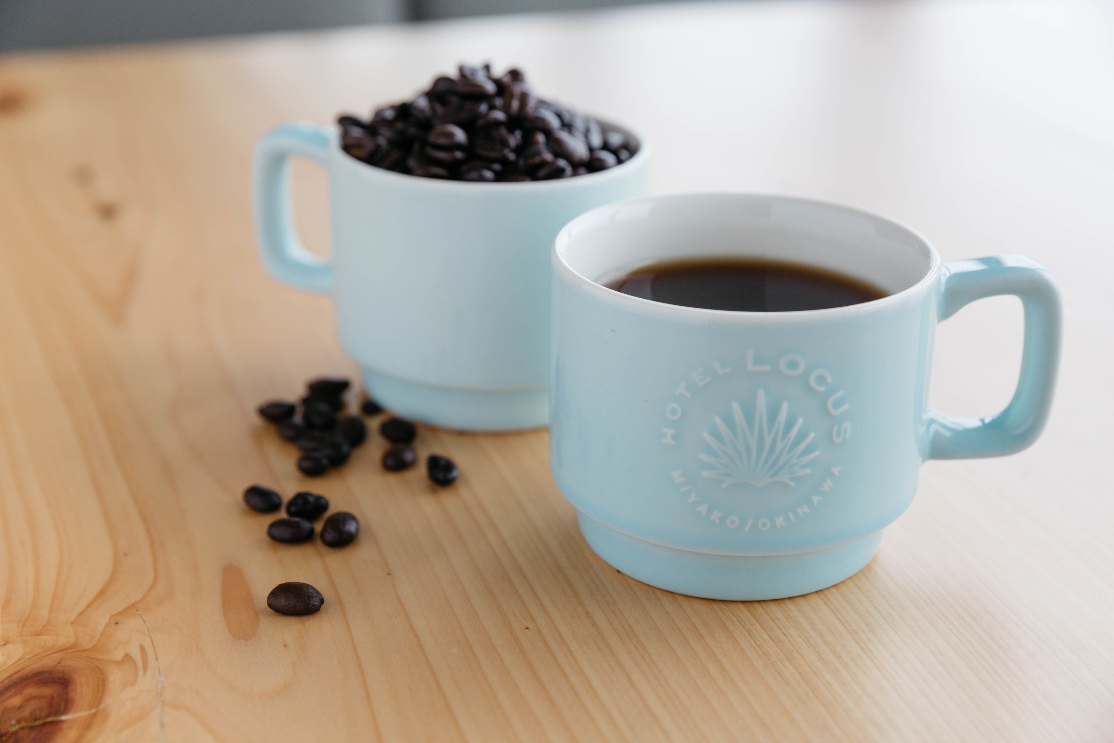 Two light blue coffee cups on a wooden table, one with coffee and the other with coffee beans.