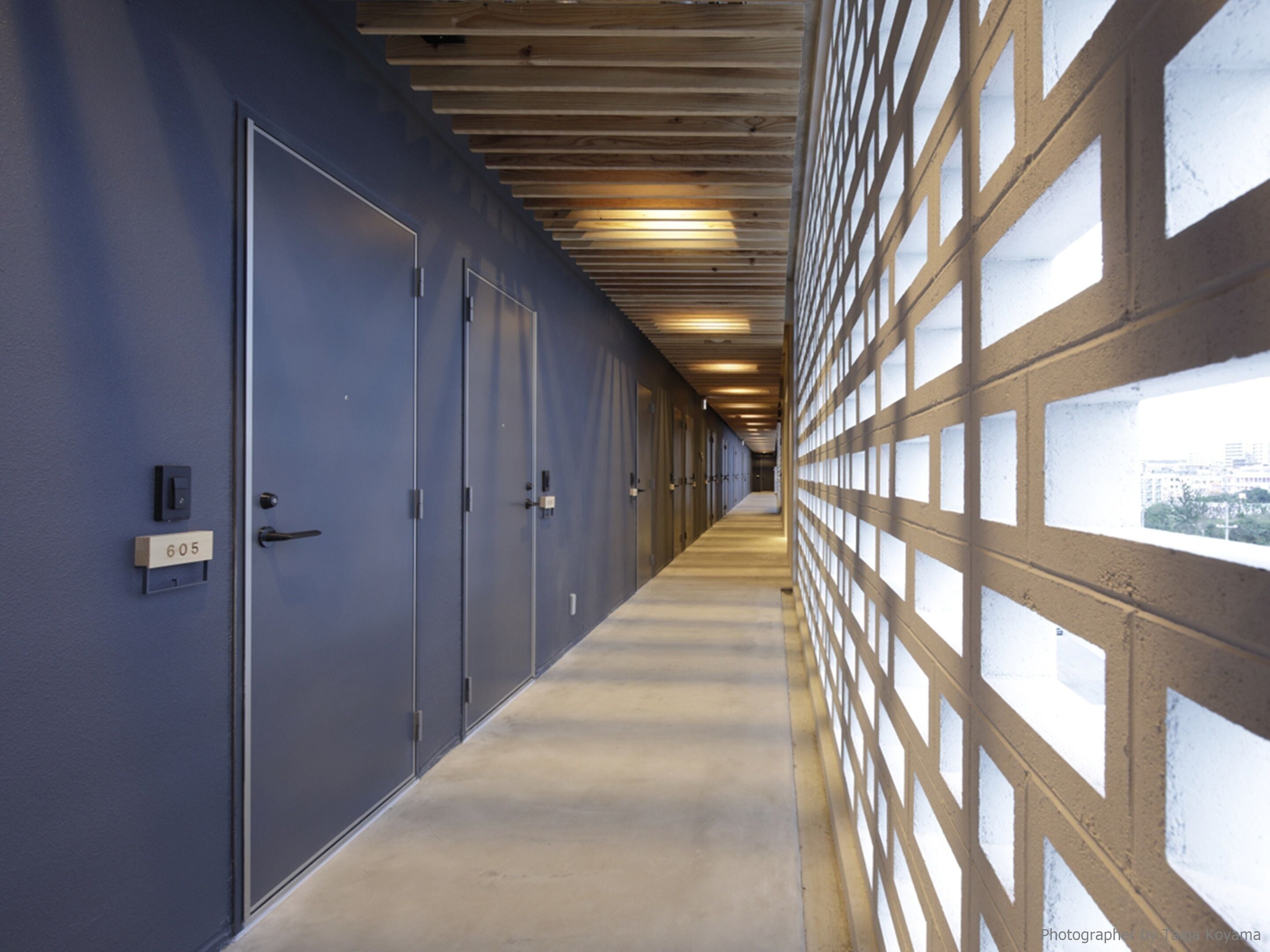 A corridor with a blue wall, numbered doors, and a wooden ceiling.