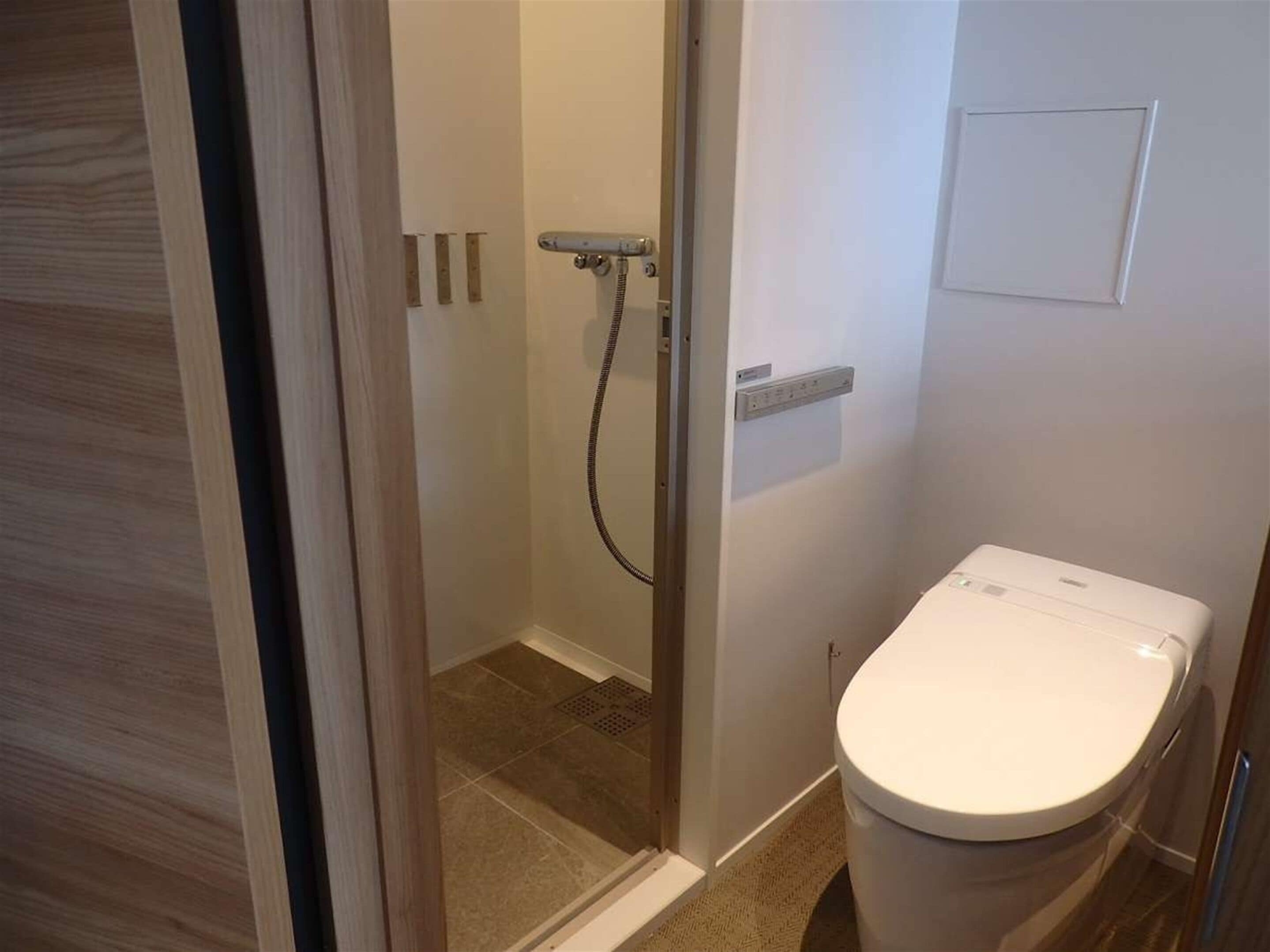 A bathroom with a shower, toilet, and a small electrical outlet on the wall.