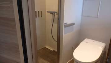A bathroom with a shower, toilet, and a small electrical outlet on the wall.
