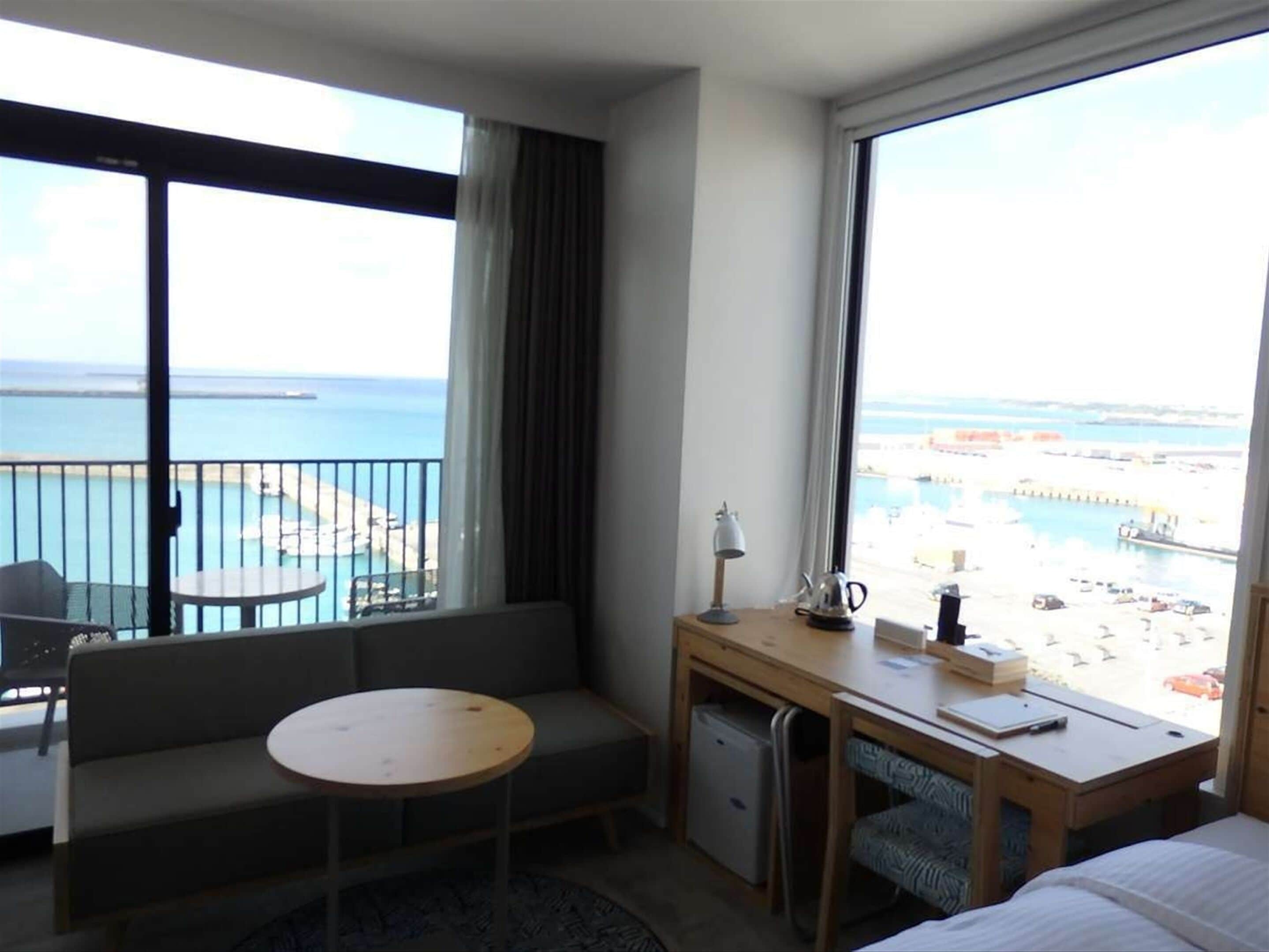 A hotel room with a balcony, a small desk, a chair, a sofa, and a bed.