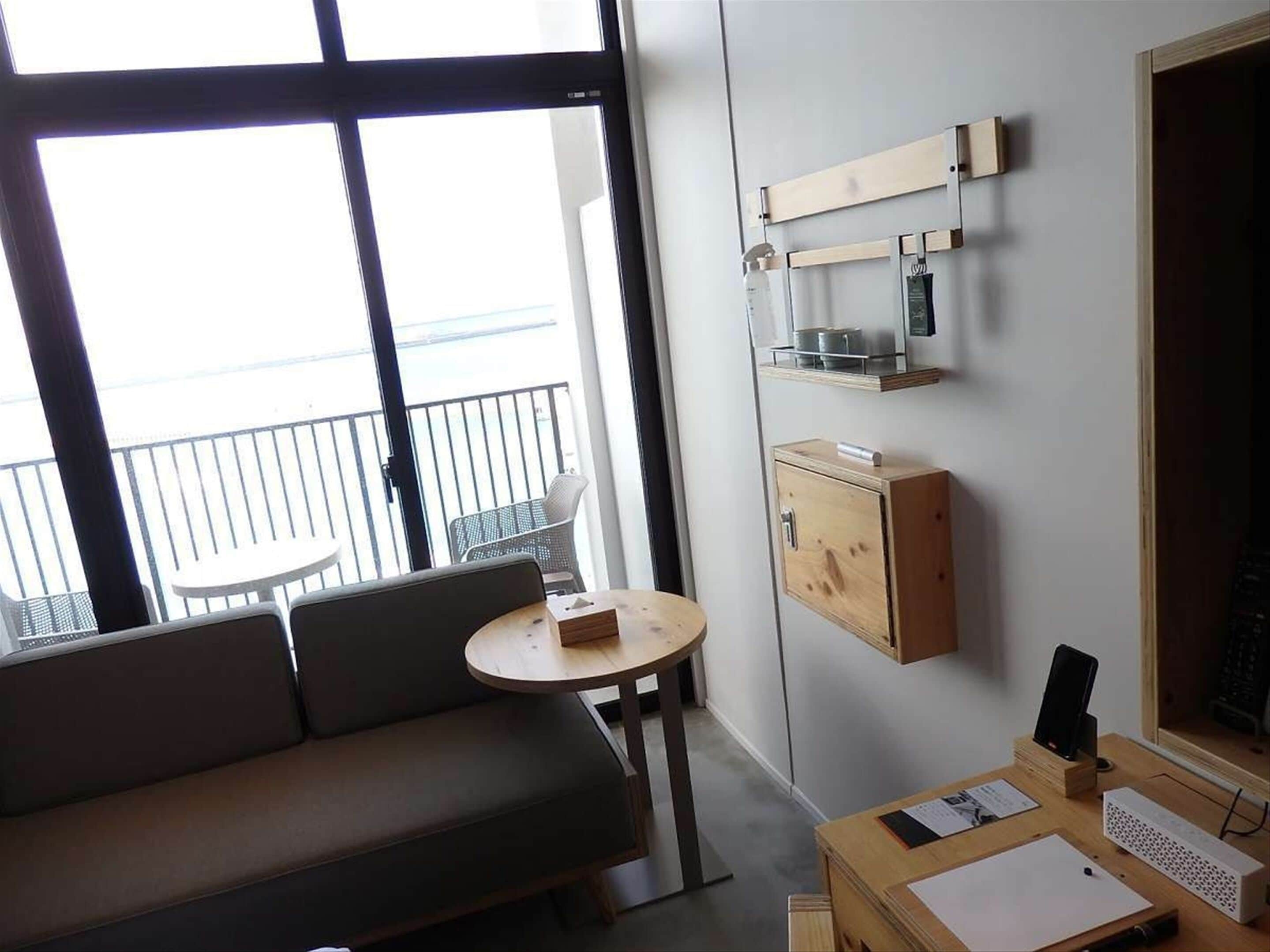 A modern room with a sofa, a small round table, a desk with a computer, and a view of the balcony.