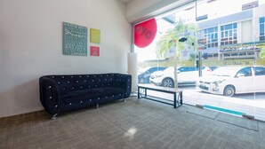 Un área de recepción con un sofá azul oscuro, un banco y un amplio ventanal con vista a coches aparcados y un edificio con señalización.