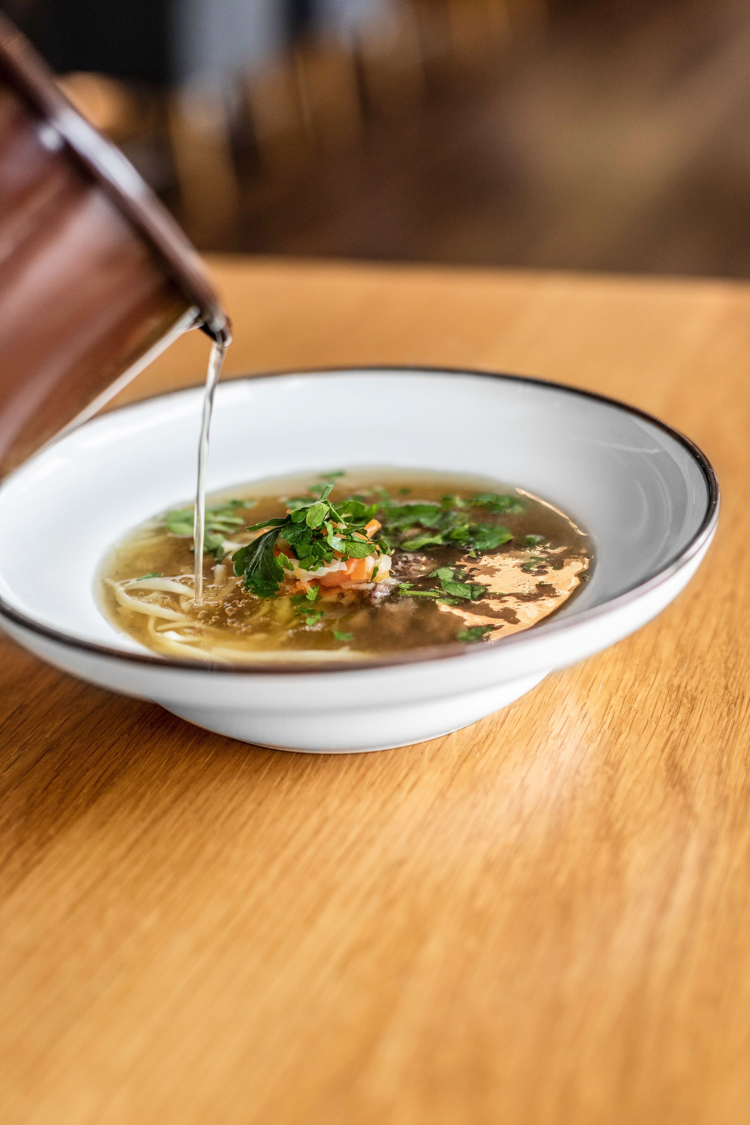 A bowl of soup with a clear broth, garnished with herbs, on a wooden table.