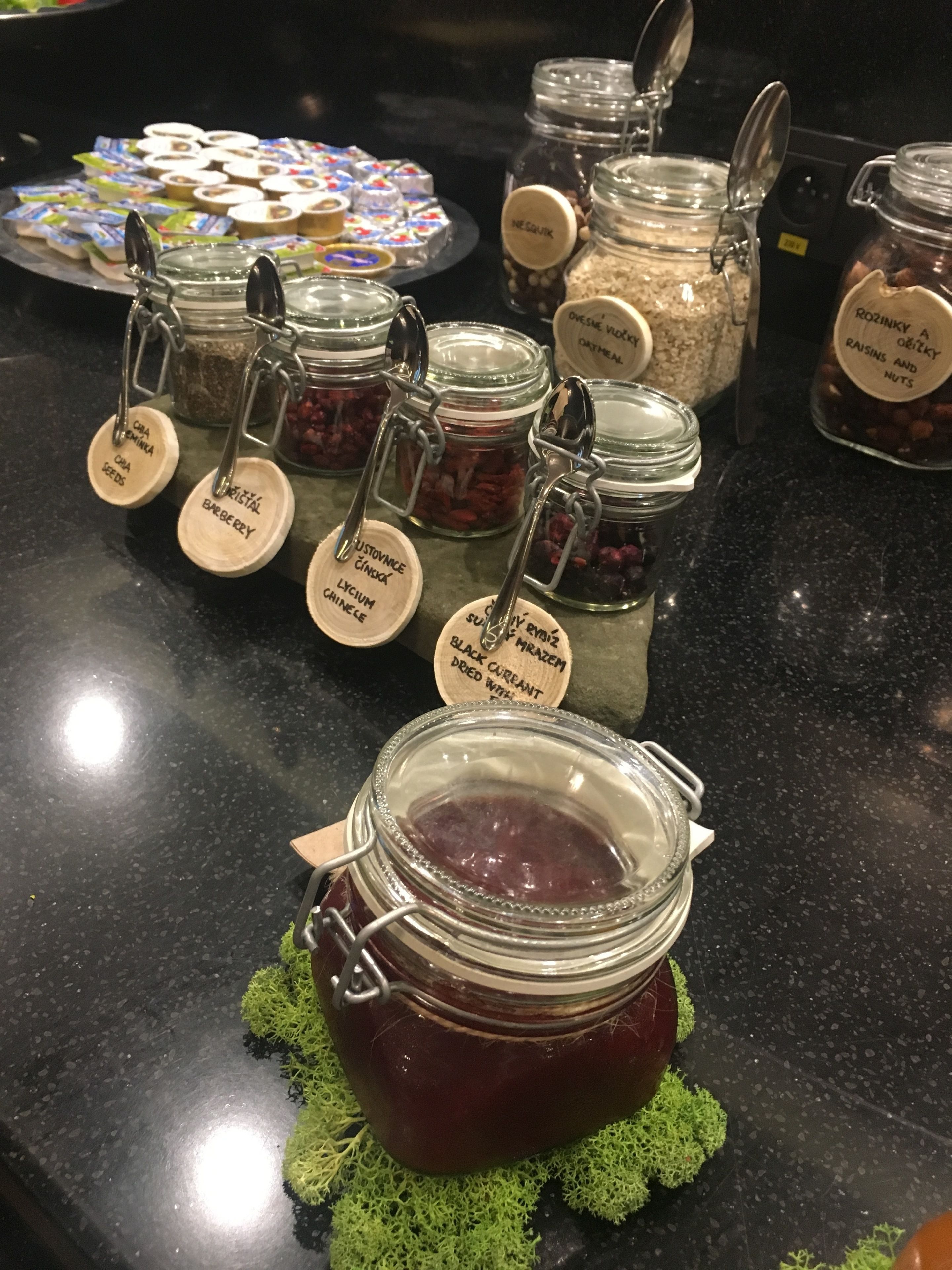Presentación de diversos alimentos en frascos con etiquetas, incluyendo un frasco de mermelada de grosellas.
