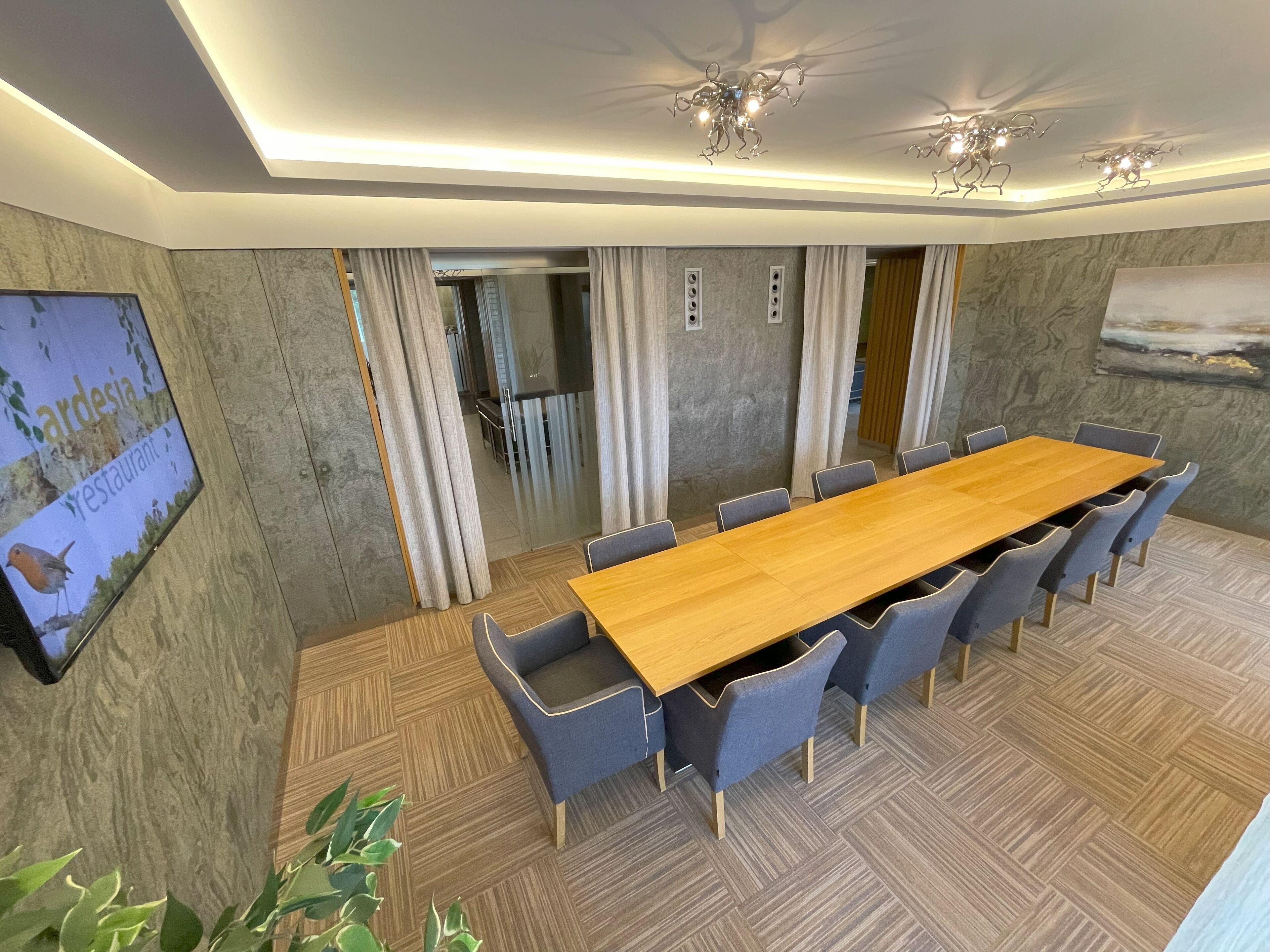 Una sala de conferencias con una larga mesa de madera, sillas tapizadas en gris y un suelo con estampado de espiga.