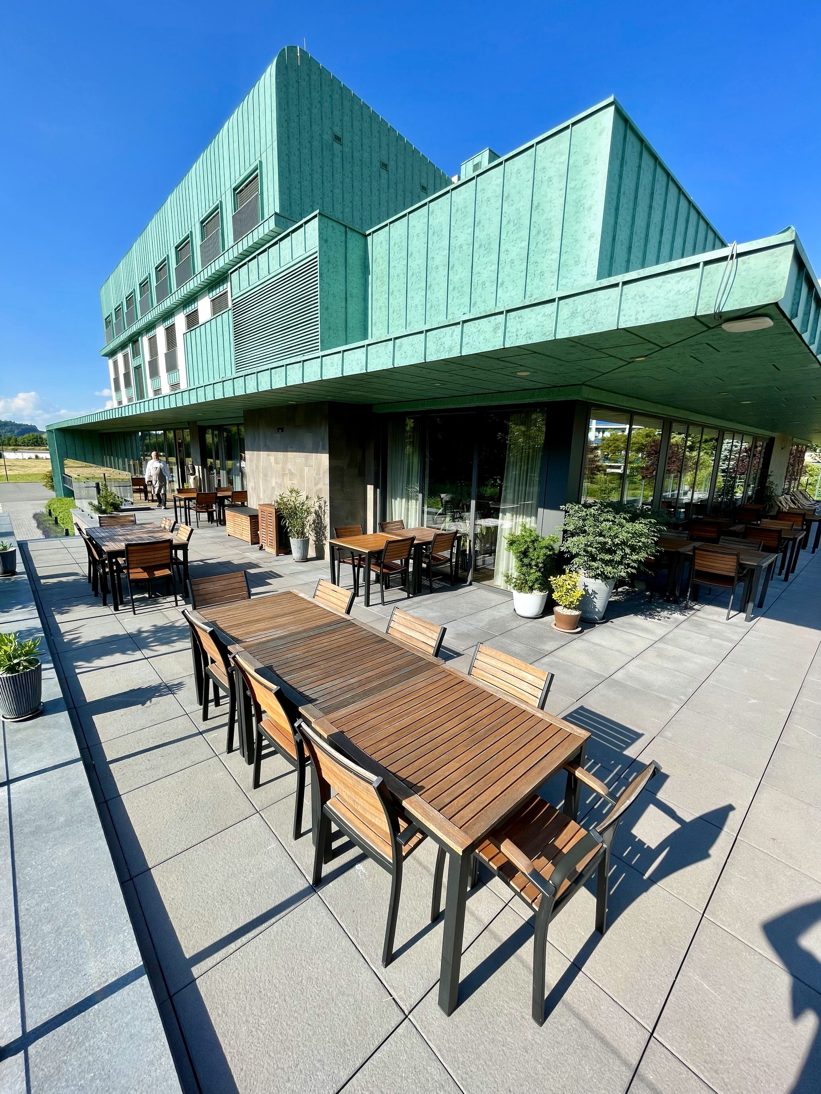 Un edificio con fachada verde y un patio con mesas y sillas de madera.