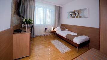 Een hotelkamer met een bed, een bureau, een televisie, een raam met gordijnen en een schilderij aan de muur.