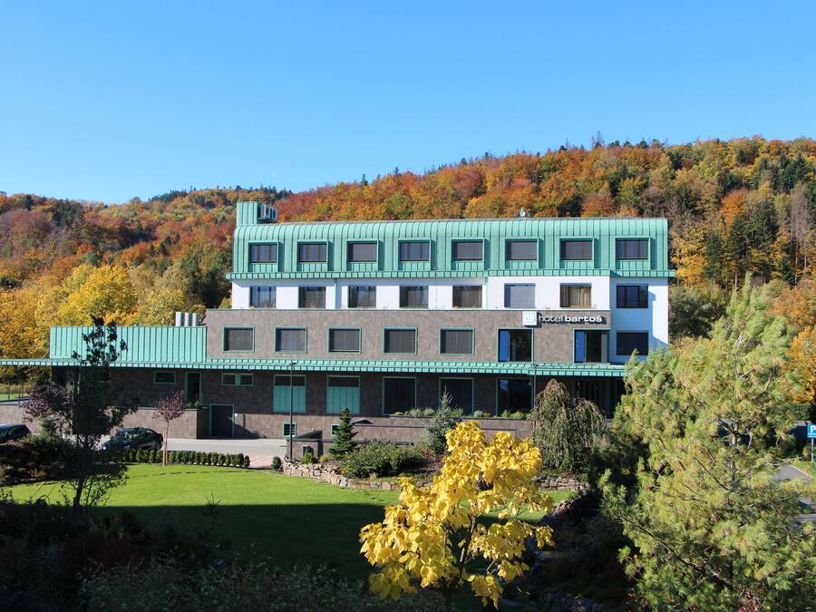Hotel de vários andares com telhado verde e paredes brancas, rodeado por folhagem de outono.
