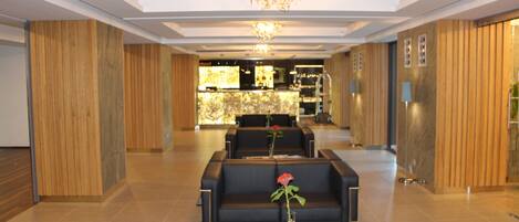 A hotel lobby with a reception desk, black sofas, a chandelier, and a rose in a vase.