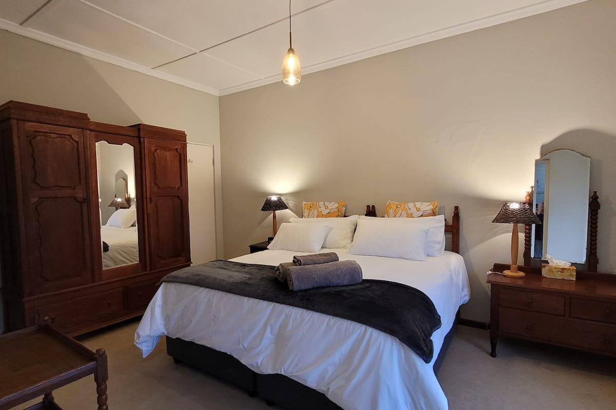 A neatly made bed with a dark headboard, a wooden wardrobe, a mirror, and two bedside lamps.
