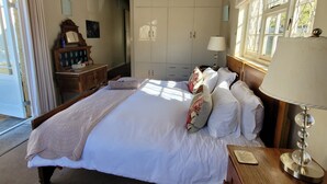 Un dormitorio con una cama grande, cabecera de madera, un armario, una mesita de noche con lámpara y una ventana con cortinas.
