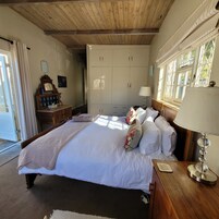 Un dormitorio con una cama grande, cabecera de madera, un armario, una mesita de noche con lámpara y una ventana con cortinas.
