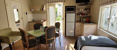 A compact room with a dining table, chairs, a bed, a TV, and a refrigerator.