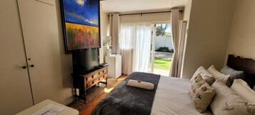 Una habitación de hotel con una cama, un televisor sobre un mueble de madera, un cuadro en la pared y vista al jardín por la ventana.