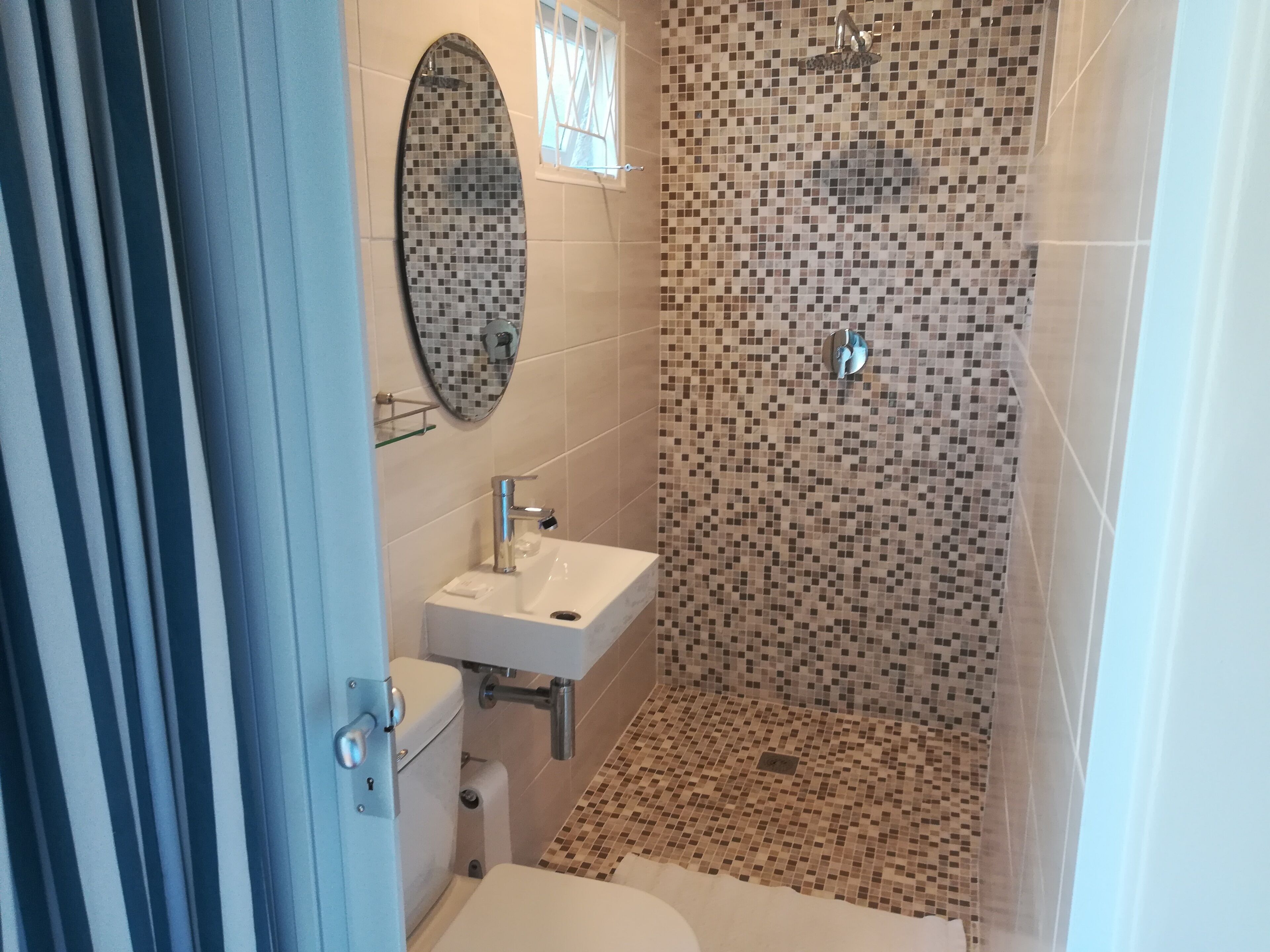 A bathroom with a tiled shower, a sink, a toilet, and a mirror.