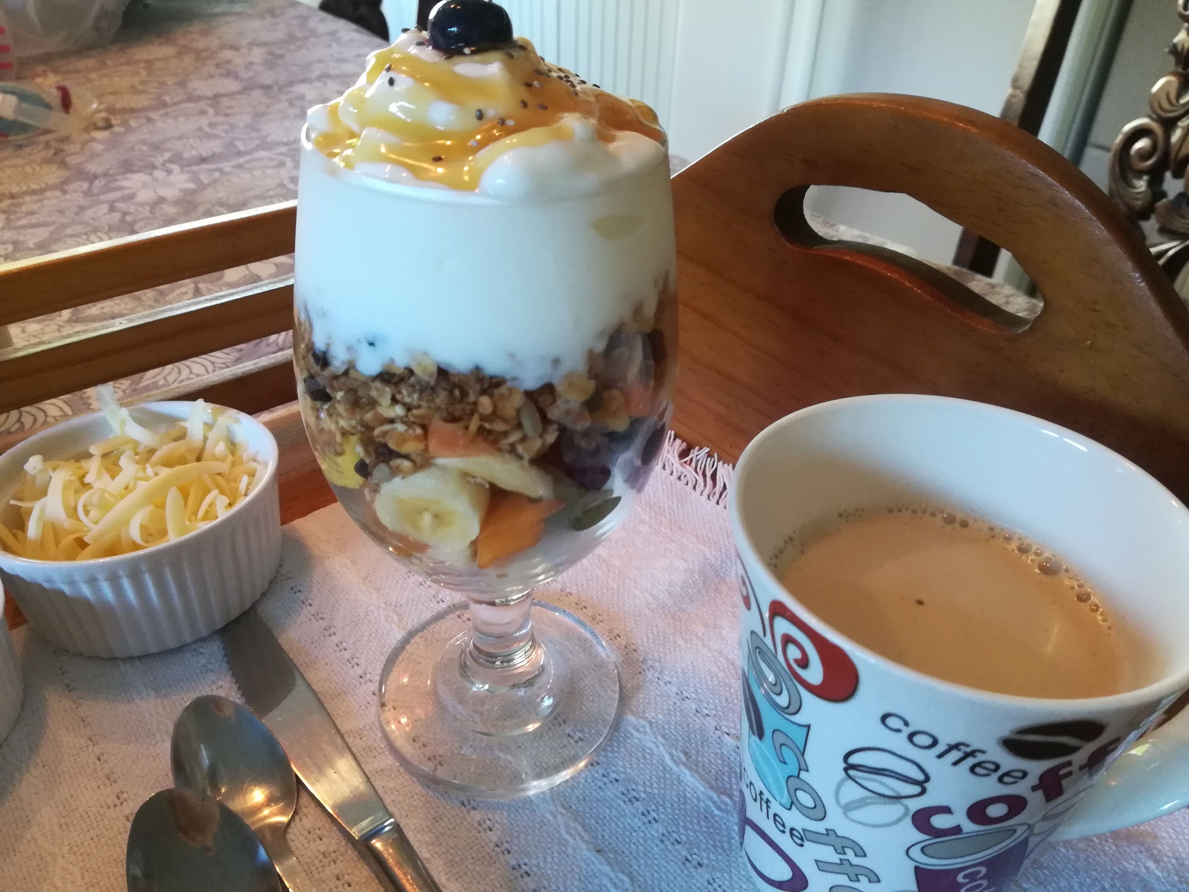 A dessert in a glass, a coffee cup, and a bowl of fruit on a table.
