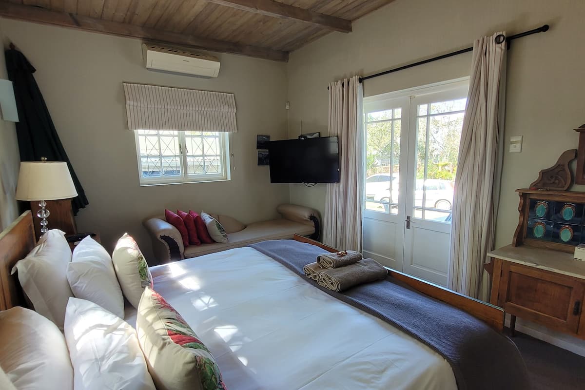 A bedroom with a large bed, a sofa, a TV, and a window with curtains.
