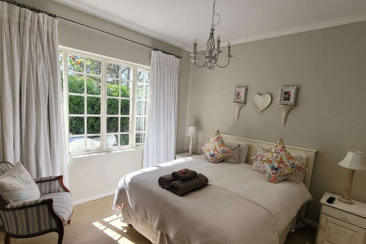 A bedroom with a large bed, a chair, a nightstand, and a window with curtains.