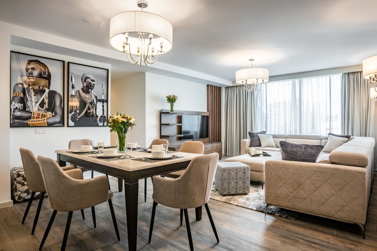 A modern living room with a dining area, featuring a sofa set, a TV, and artwork on the wall.