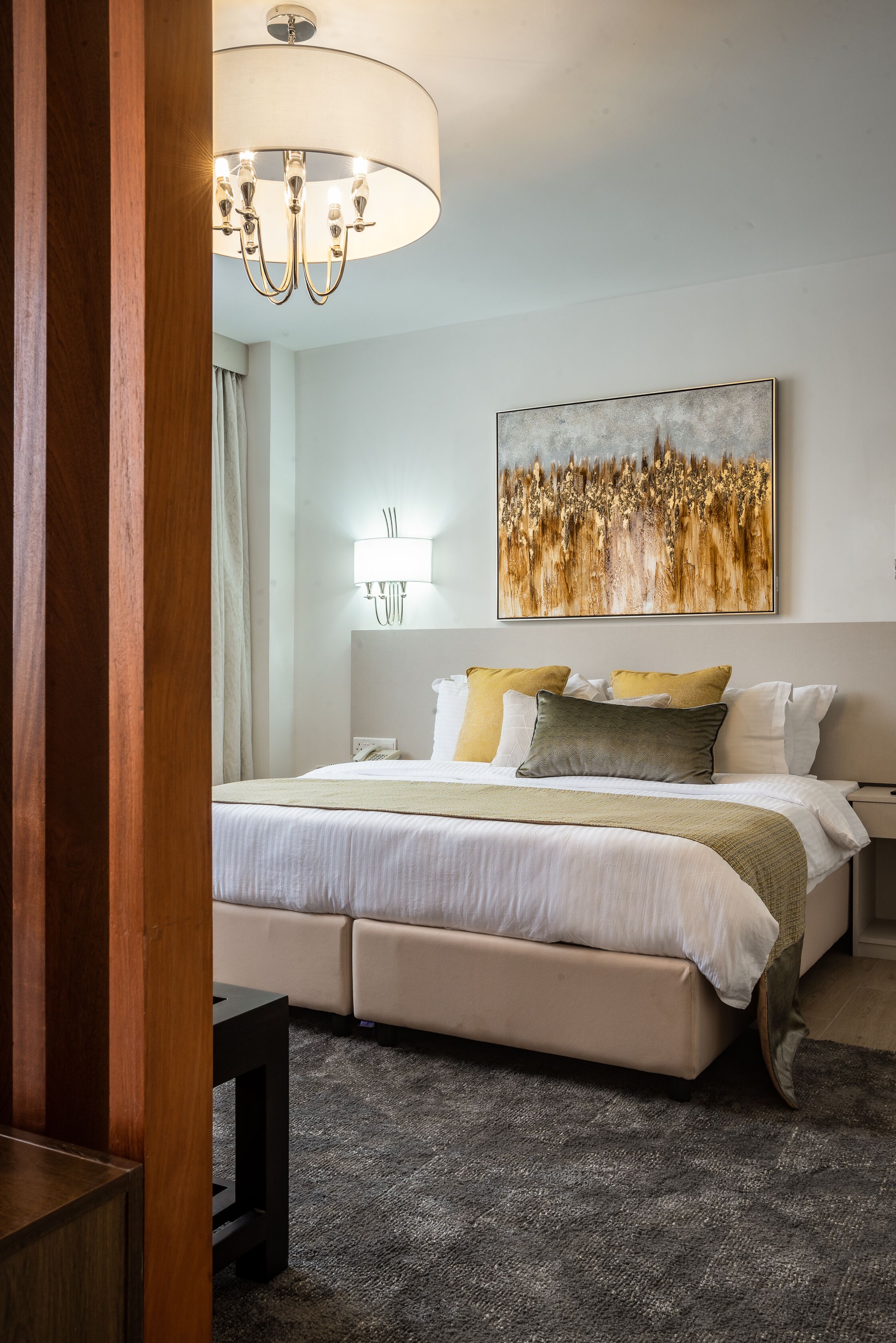 A hotel room with a large bed, a bedside table, a lamp, and a painting on the wall.