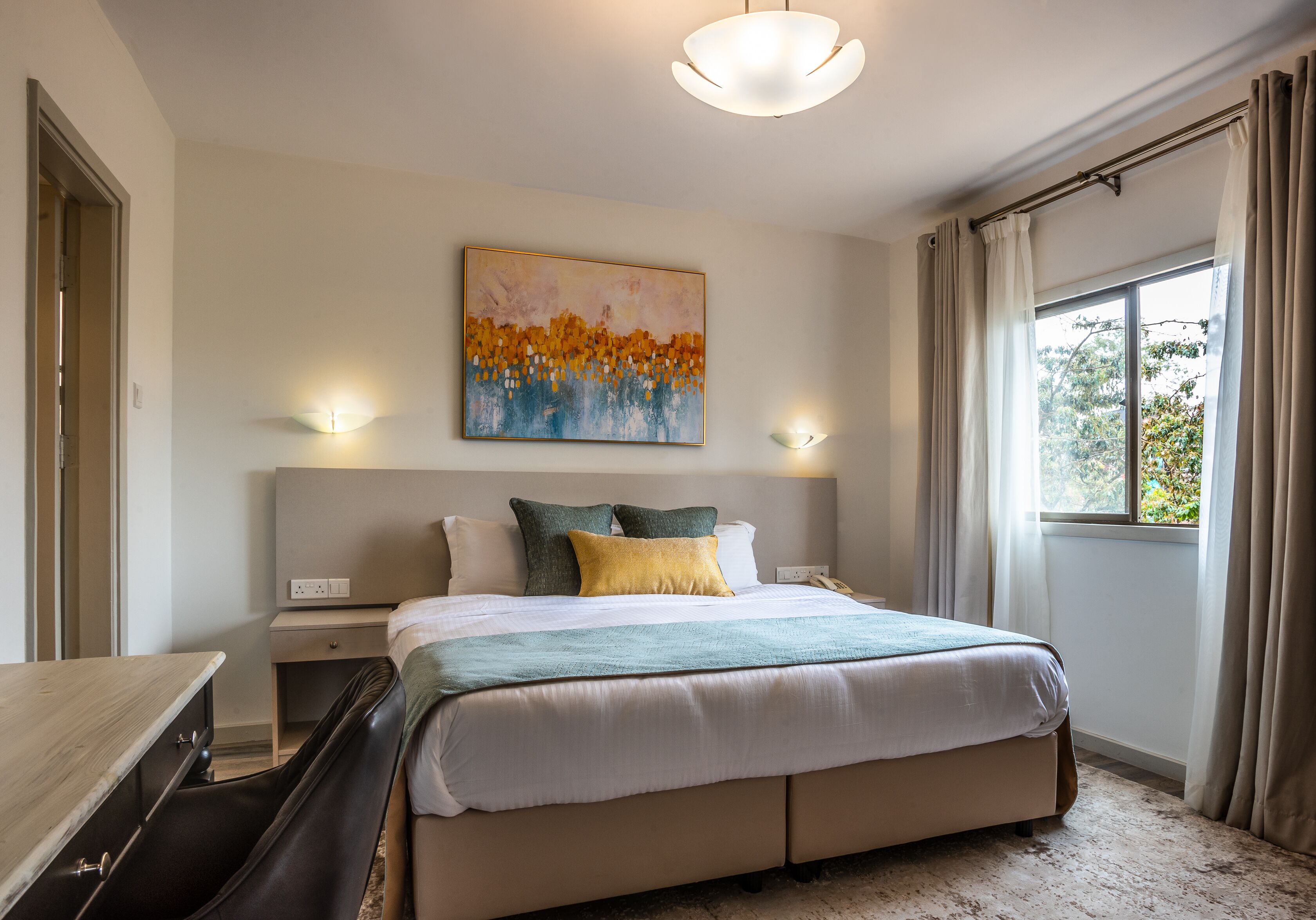 A hotel room with a bed, bedside table, lamp, and a painting on the wall.