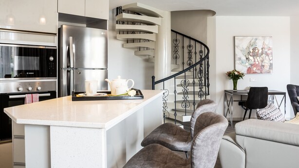 A modern kitchen with a central island, bar stools, a dining area with a table and chairs, and a staircase with a railing. - Yaya Hotel and Apartments (Nairobi)