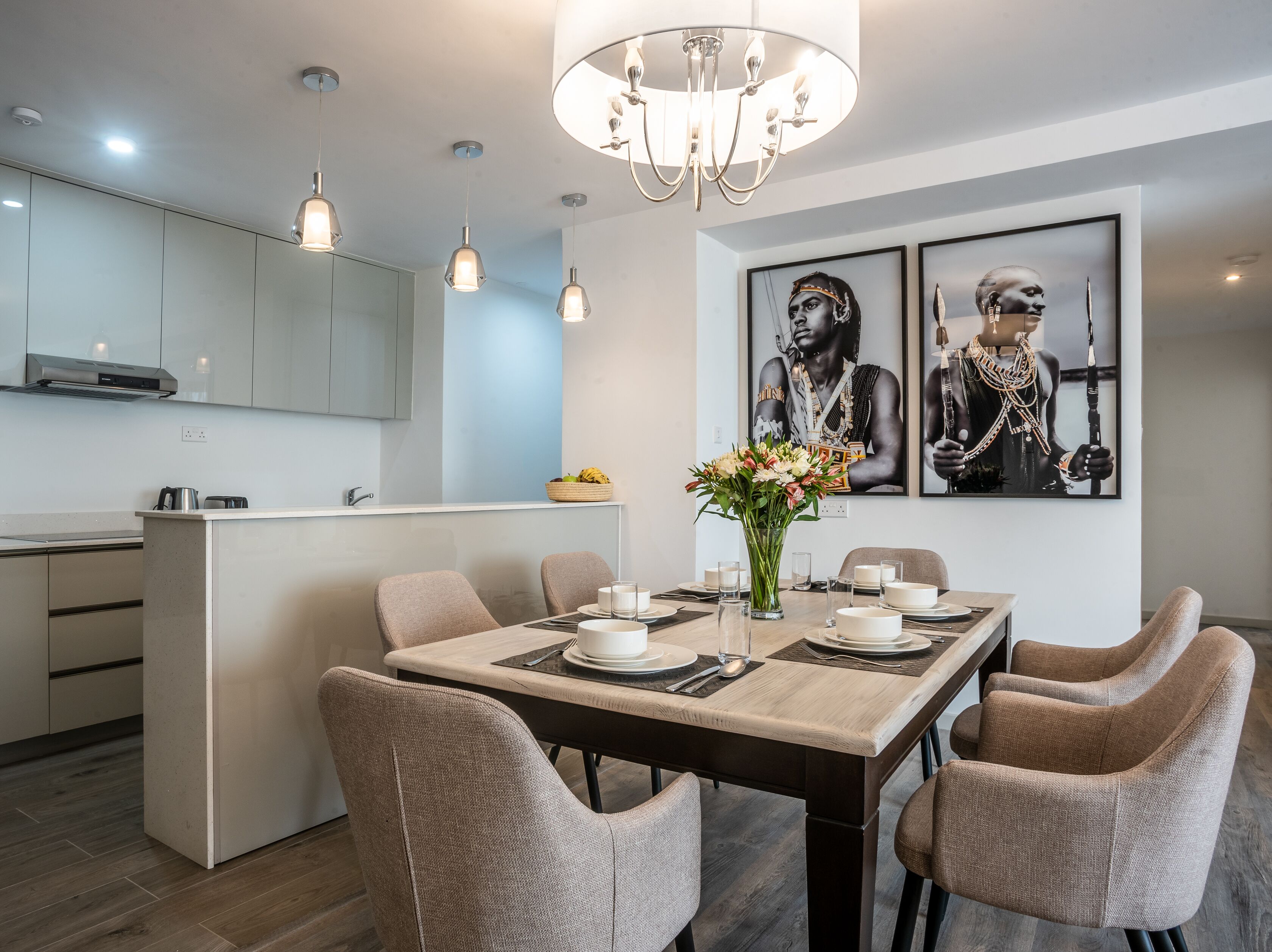 Una cocina moderna con una isla central, iluminación colgante y una zona de comedor con una mesa para cuatro.