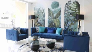 A modern living room with a blue sofa set, a glass coffee table, and a large botanical mural on the wall. - Yaya Hotel and Apartments (Nairobi)
