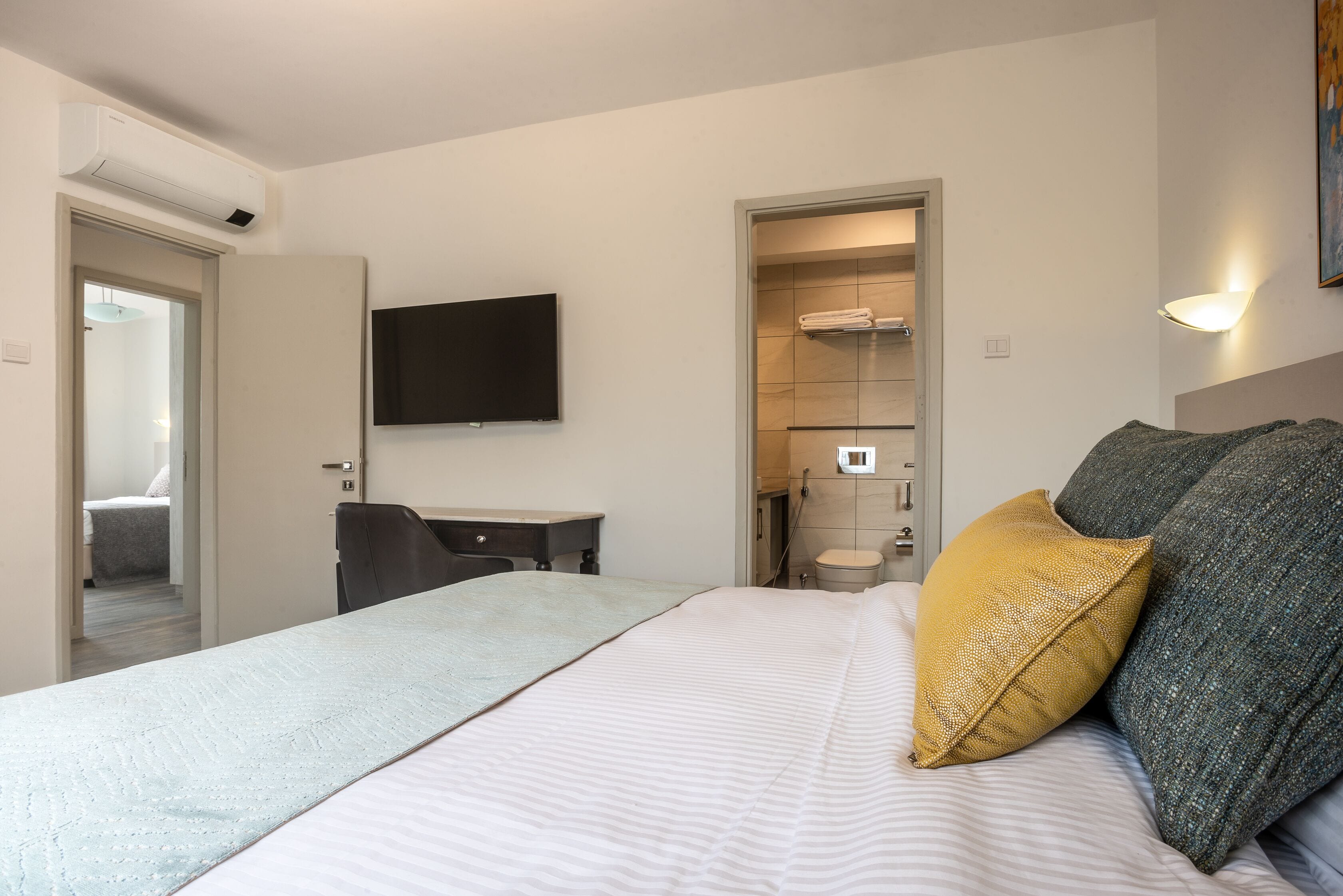 A hotel room with a bed, a desk, a TV, and a bathroom visible through an open door.
