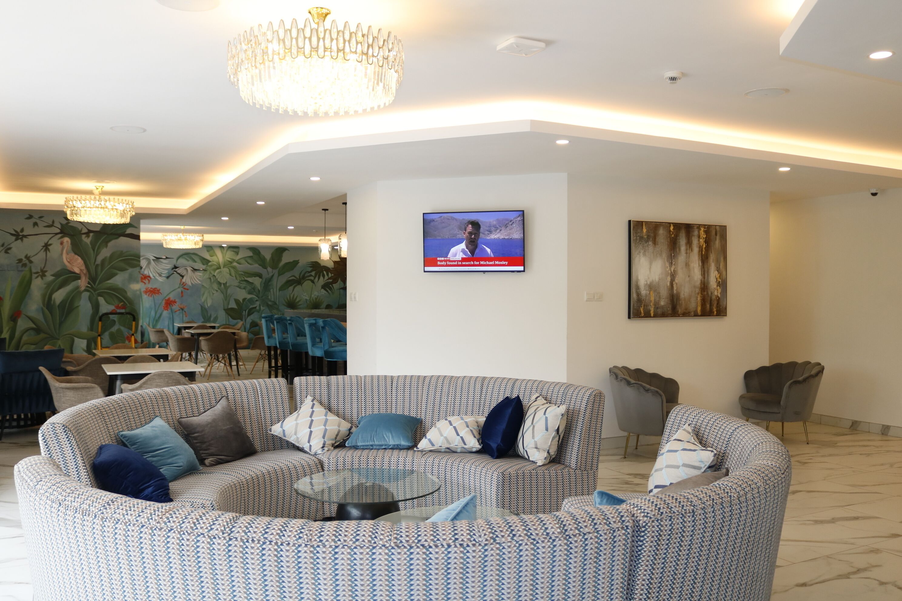 A modern living room with a patterned sofa, a glass coffee table, and a television mounted on the wall.