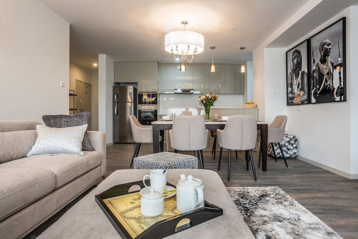 A modern living room with a sofa, ottoman, and a tray with teapots.