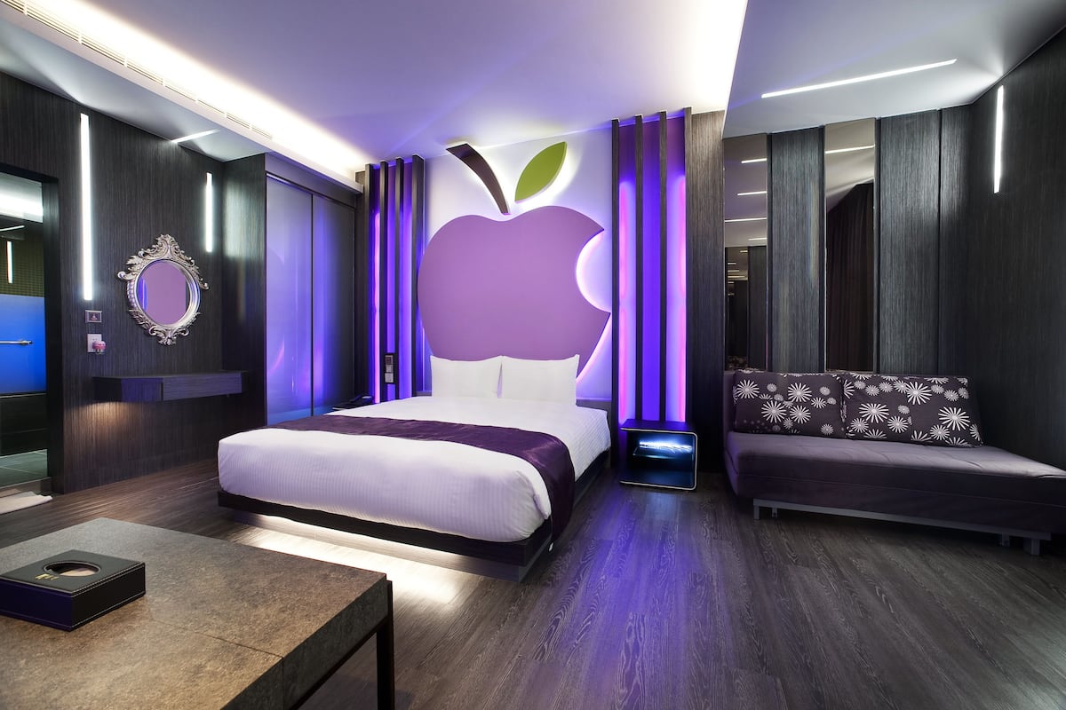 Quarto de hotel moderno com uma cama grande, um sofá, um espelho e uma parede com o logotipo da Apple.