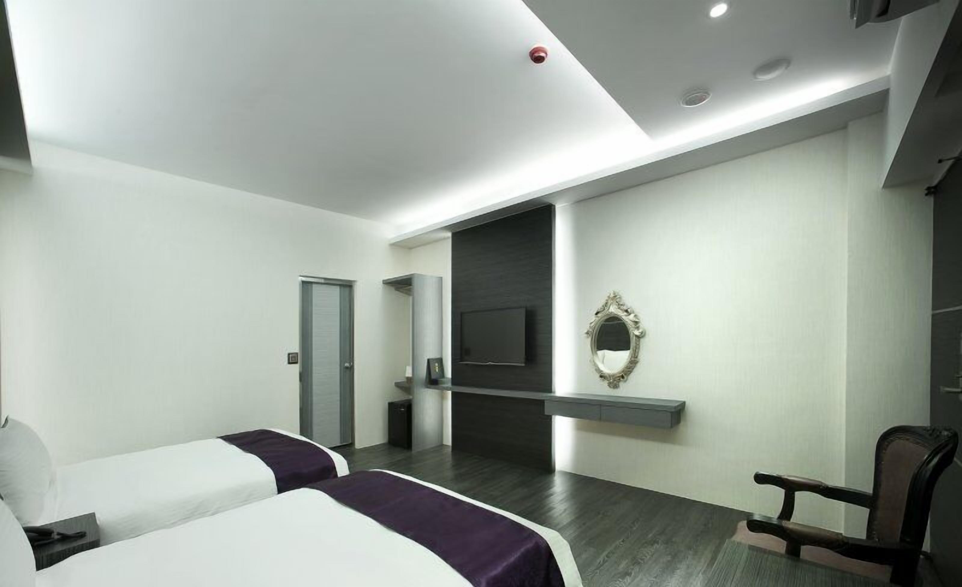 A modern hotel room with two beds, a TV, a mirror, and a wooden chair.