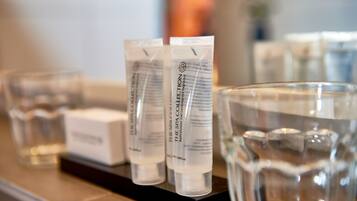 A row of spa products on a shelf, including bath/shower gel and a glass of water.
