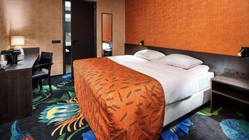 A hotel room with a bed, a desk with a lamp, a chair, and a mirror.